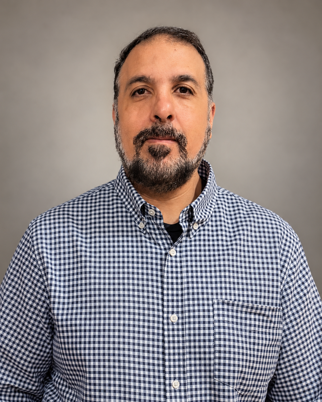 Professional portrait of Wajid Mirza wearing a checked shirt against a neutral gray background.
